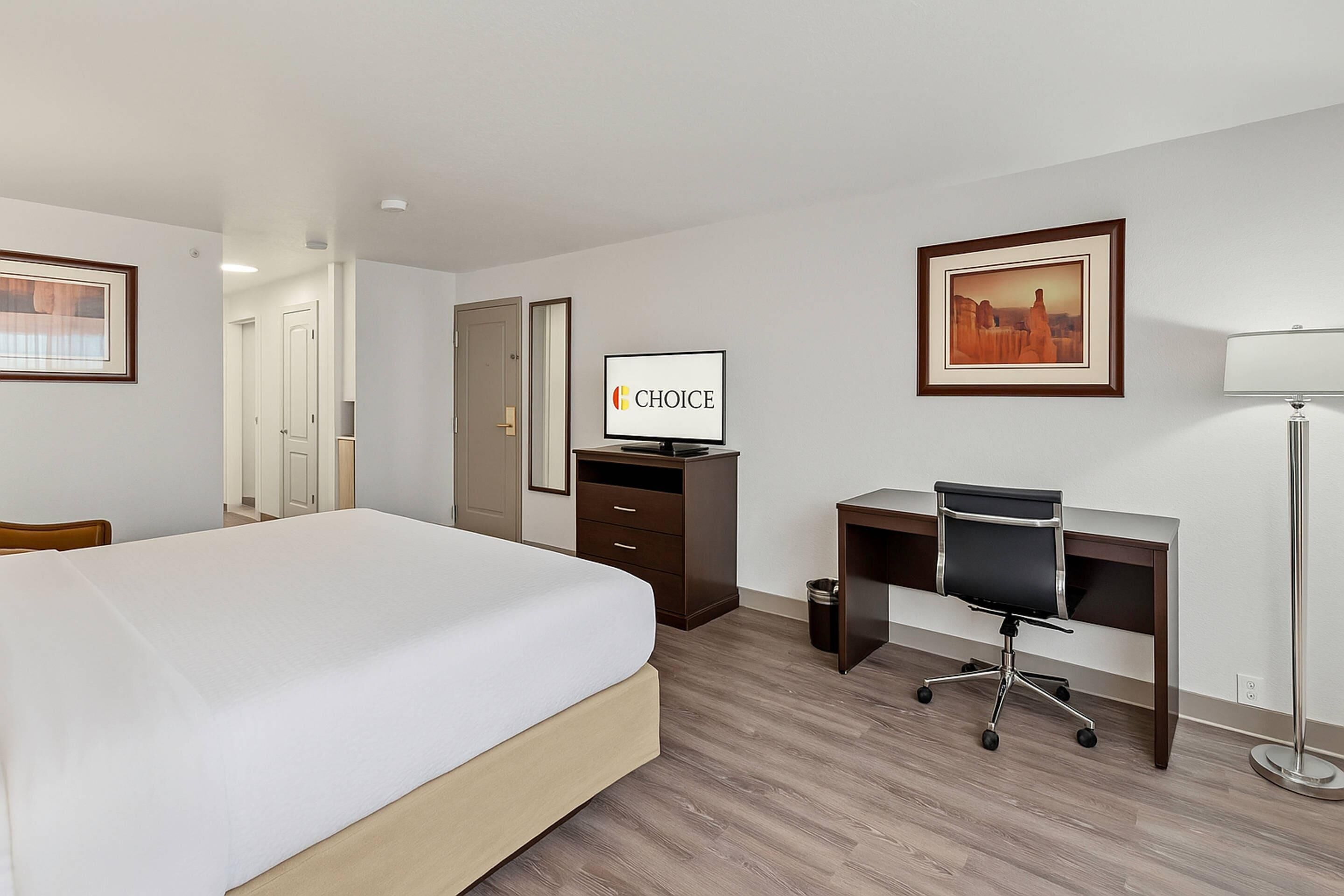 Une chambre d’hôtel avec un lit, un bureau, une chaise, une télévision et des tableaux encadrés aux murs.