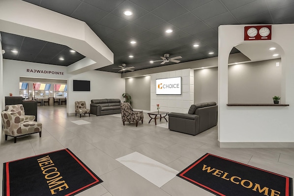 A modern hotel lobby with a reception desk, seating area, and a 'Welcome' mat.