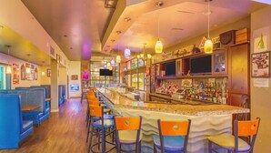 A bar with a long counter, bar stools, and a television screen. - Suburban Studios Salt Lake City Airport (Salt Lake City)