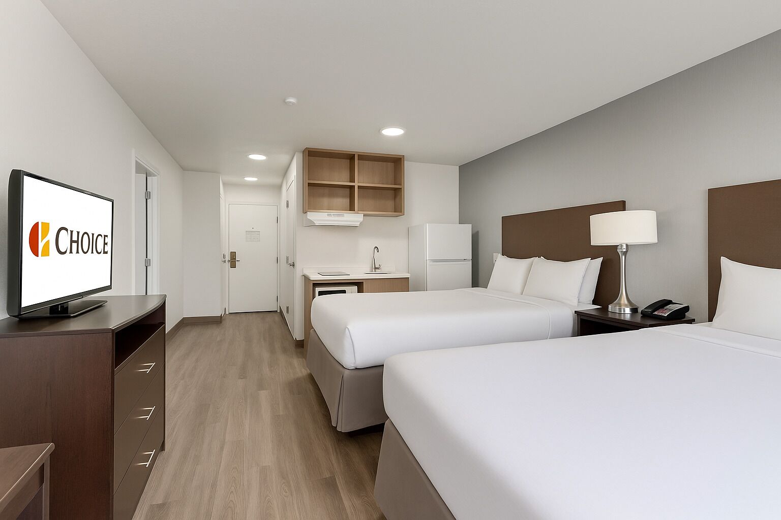 Habitación de hotel con dos camas, televisión, escritorio con silla, refrigerador y microondas.