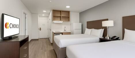 Habitación de hotel con dos camas, televisión, escritorio con silla, refrigerador y microondas.