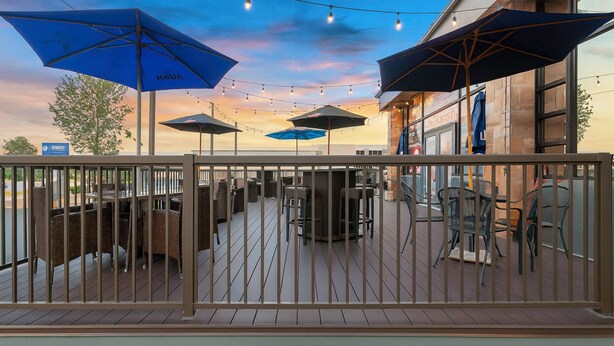 An outdoor patio with tables and chairs, covered by blue umbrellas, and string lights. - Suburban Studios Salt Lake City Airport (Salt Lake City)