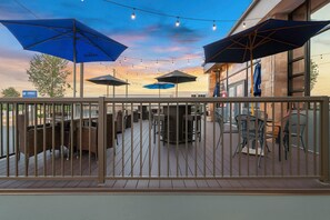 Une terrasse extérieure avec des tables et des chaises, protégée par des parasols bleus et illuminée de guirlandes lumineuses.