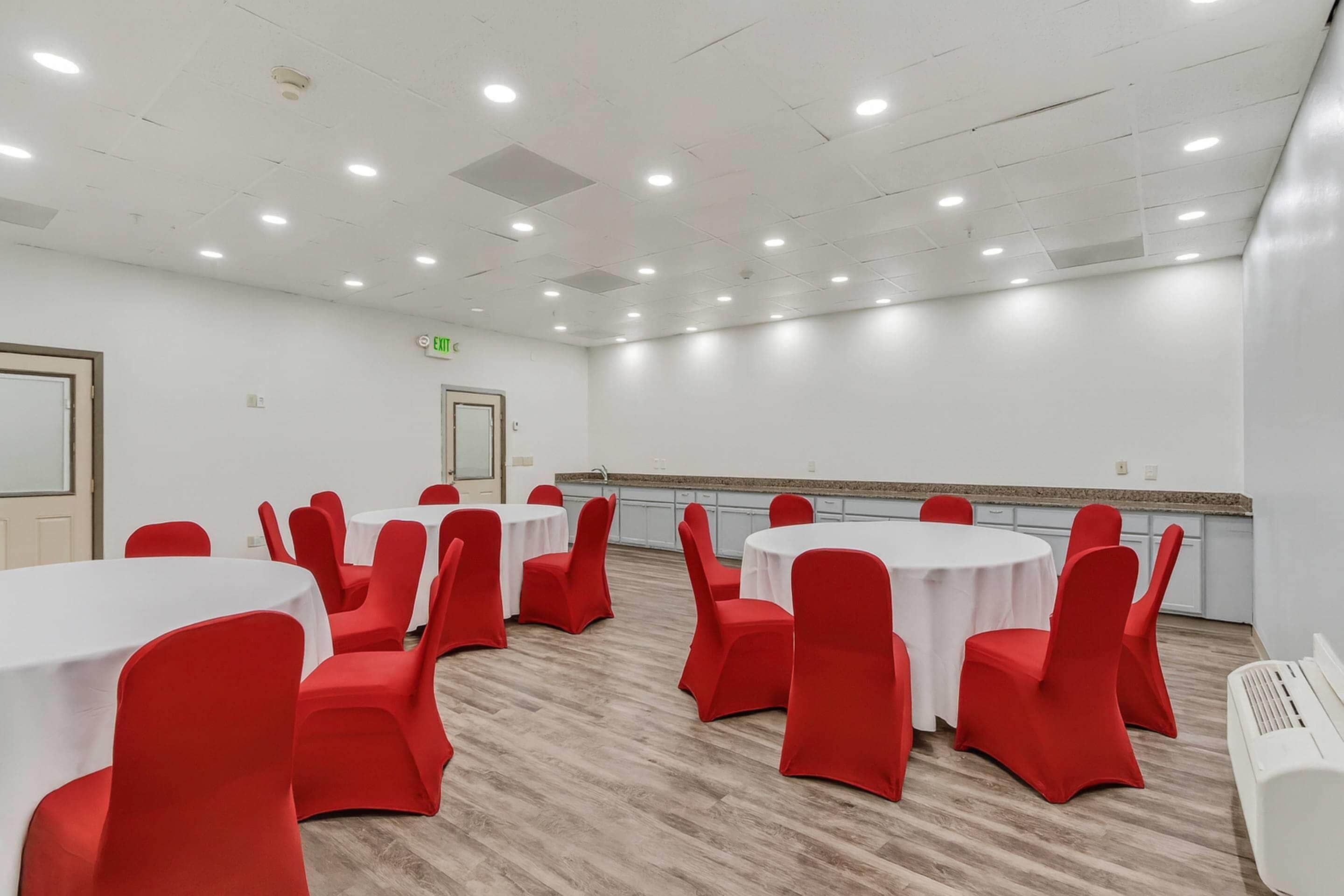 A conference room with round tables and red chairs, white walls, and a ceiling with recessed lighting.