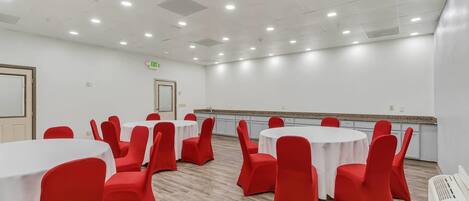A conference room with round tables and red chairs, white walls, and a ceiling with recessed lighting.
