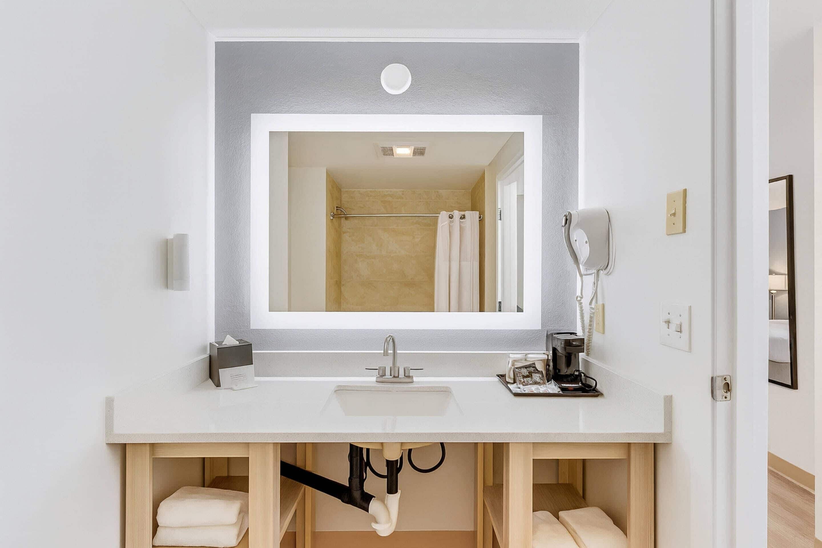 Une salle de bain moderne avec un grand miroir, un lavabo blanc et un espace pour ranger les serviettes.