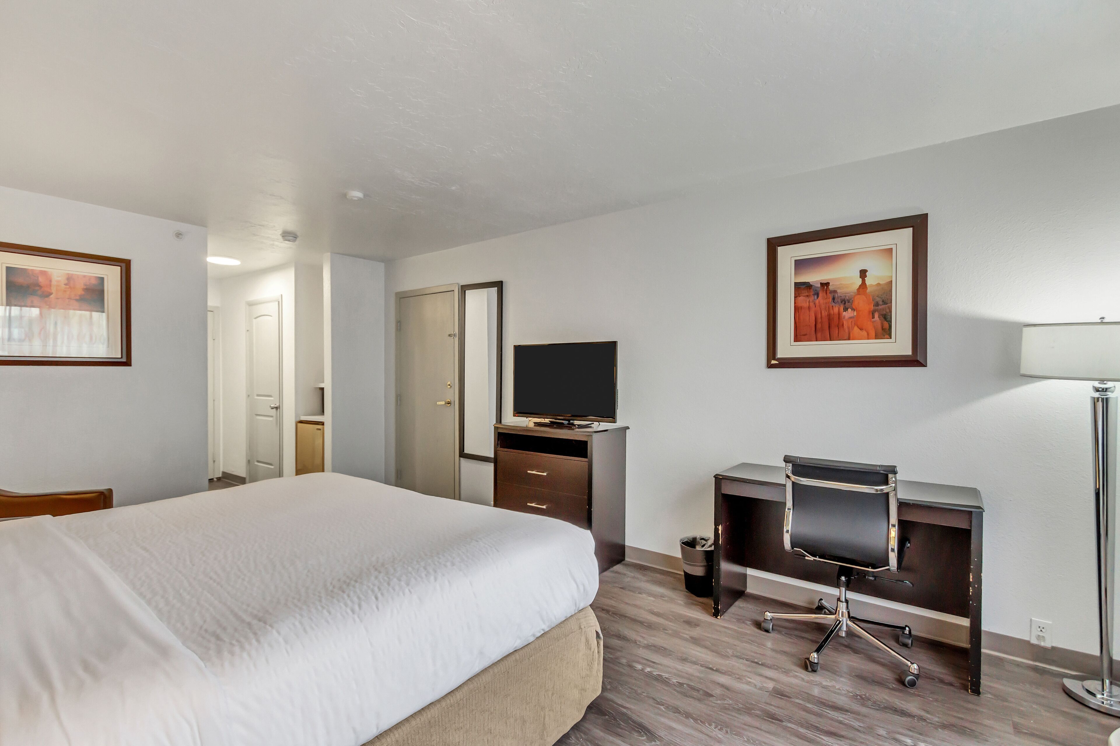 A hotel room with a bed, a desk with a chair, a television, and framed pictures on the walls.