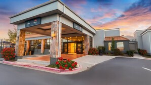 A hotel entrance with a covered area, a glass door, and red flowers in the foreground. - Suburban Studios Salt Lake City Airport (Salt Lake City)