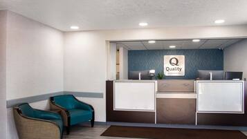 Een receptiegedeelte met een blauwe wand, een receptiebalie, twee stoelen en een bord met de tekst 'Quality by Choice Hotels'.
