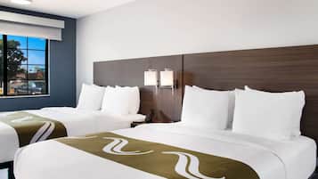 A hotel room with two beds, a large window, a nightstand, and a wall-mounted lamp.