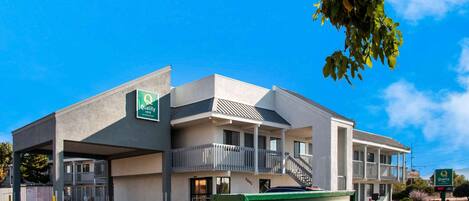 Un motel avec une enseigne verte indiquant « Entrée », un espace de stationnement couvert et un ciel d’un bleu limpide.