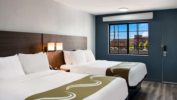 Ein Hotelzimmer mit zwei Betten, einem großen Fenster und Blick auf umliegende Gebäude.