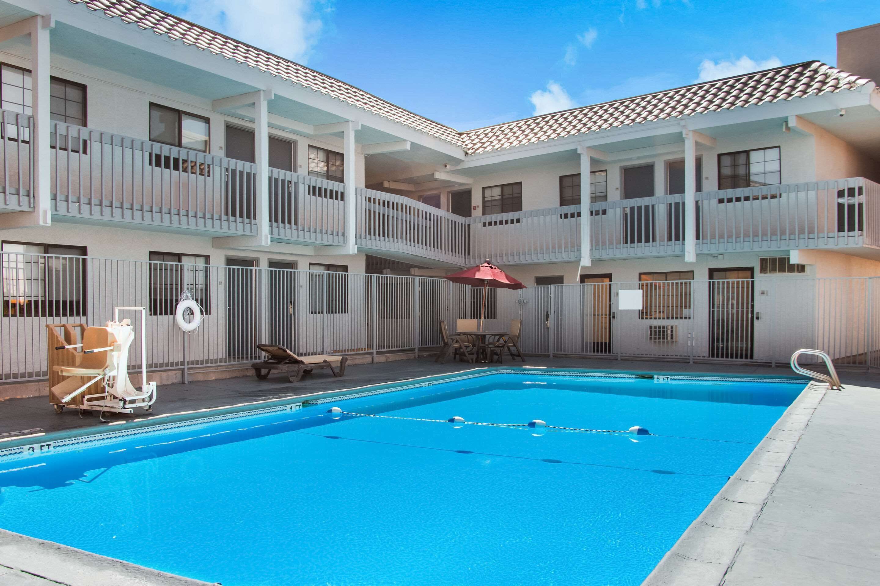 A hotel with a swimming pool, outdoor seating, and a covered patio area.