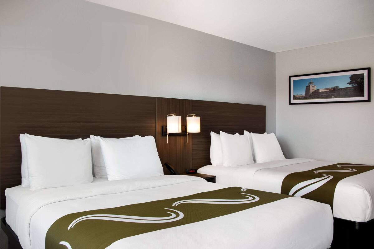 Une chambre d’hôtel avec deux lits, une tête de lit en bois, une table de chevet, une lampe et un tableau encadré au mur.