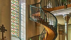 Ein Kircheninneres mit Wendeltreppe, Kirchenbänken, Buntglasfenstern und religiösen Figuren.