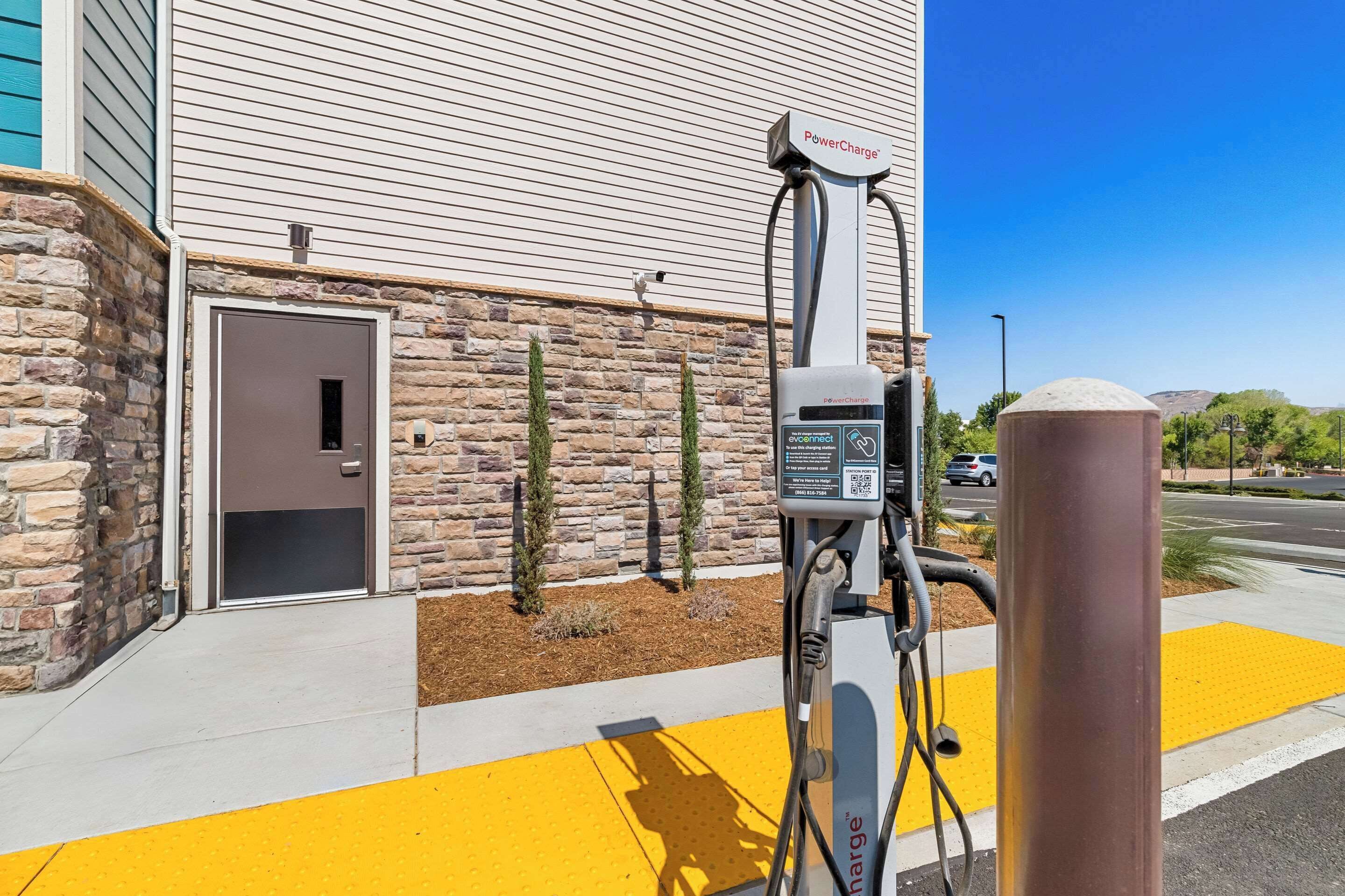 Una estación de carga para vehículos eléctricos PowerCharge frente a un edificio con paredes de piedra y una puerta.