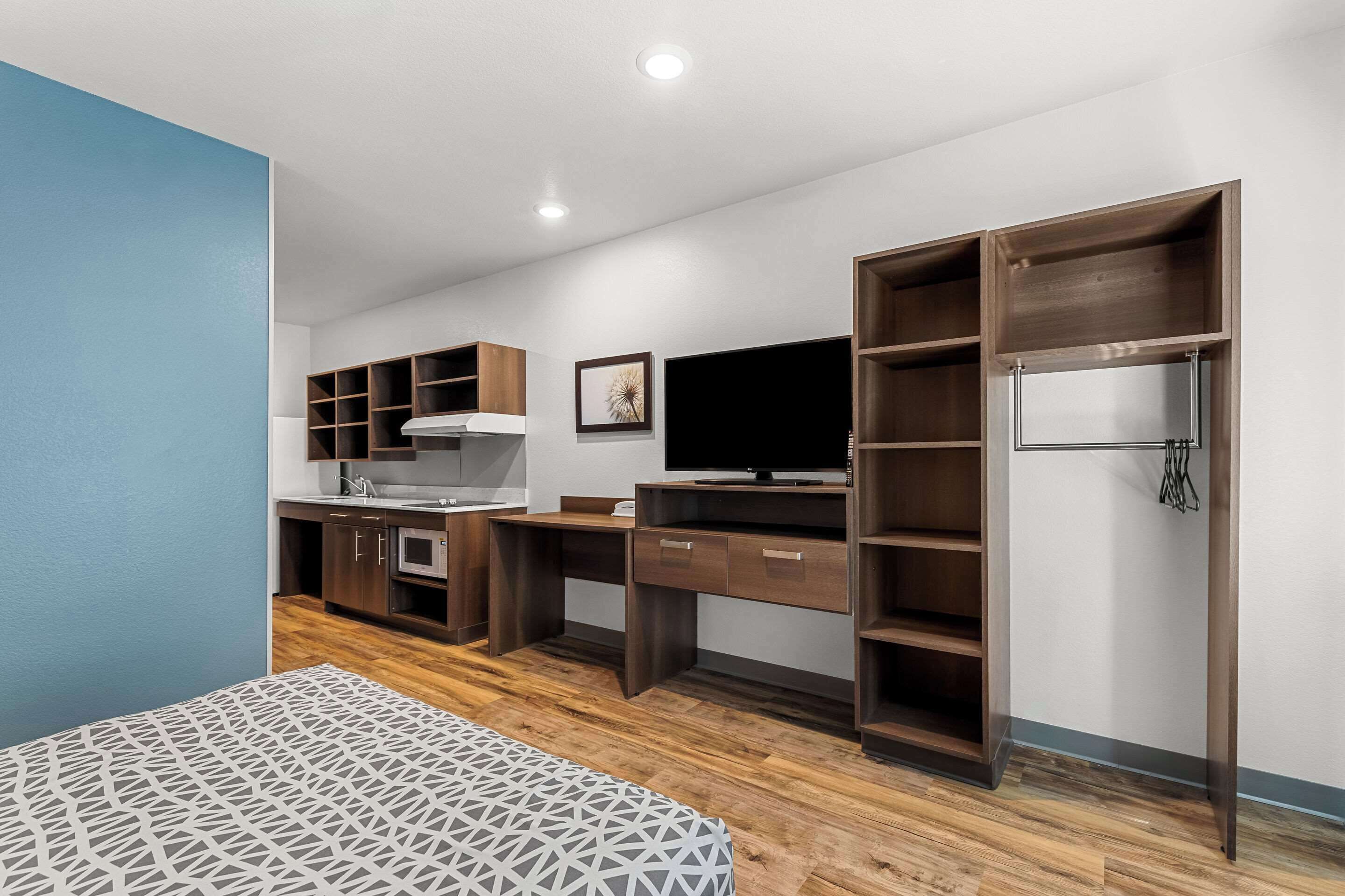 A modern bedroom with a bed, a desk, a television, and built-in shelving.