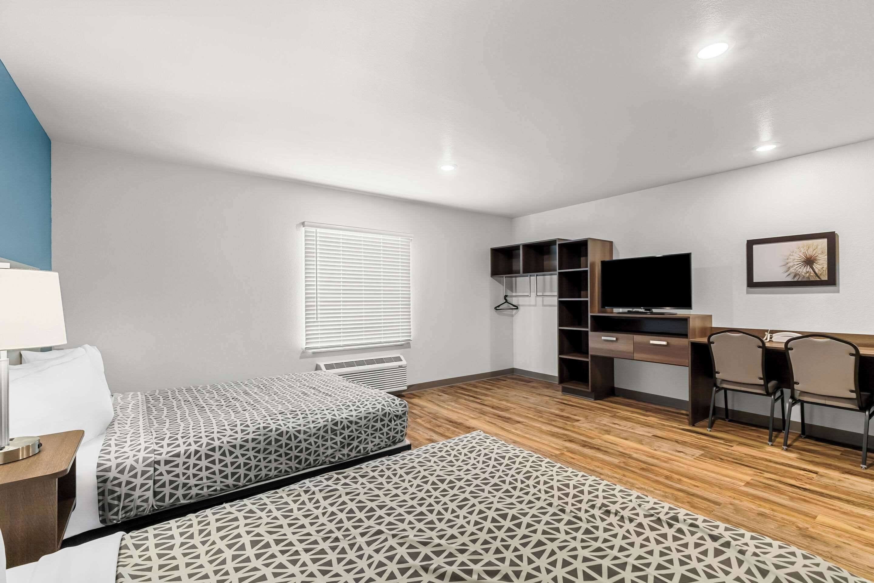 Une chambre avec deux lits, un bureau, une chaise, une télévision et une fenêtre avec des stores.