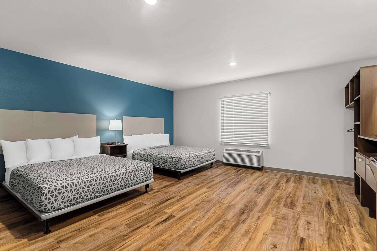Habitación de hotel con dos camas, una pared de acento azul, una ventana con persianas, un calentador y un armario de madera.