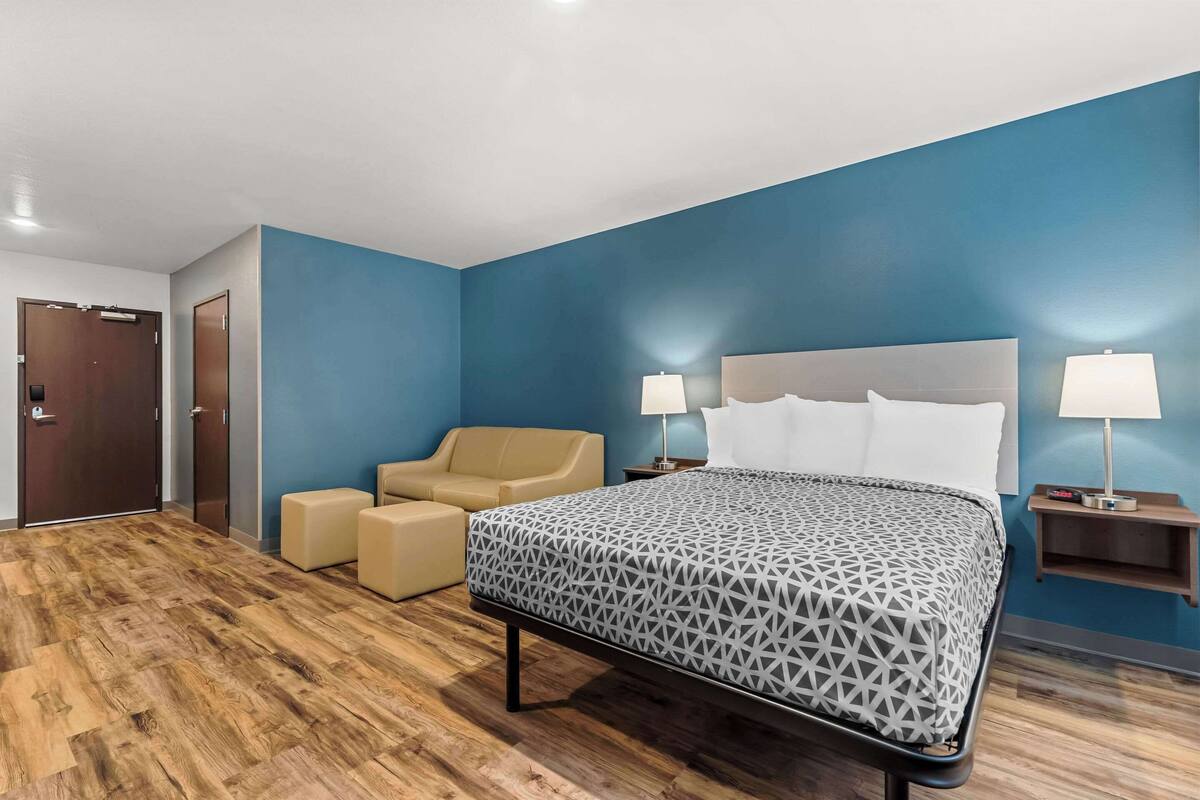 Una habitación de hotel con una cama, dos mesitas de noche con lámparas, un sofá y suelo de madera.