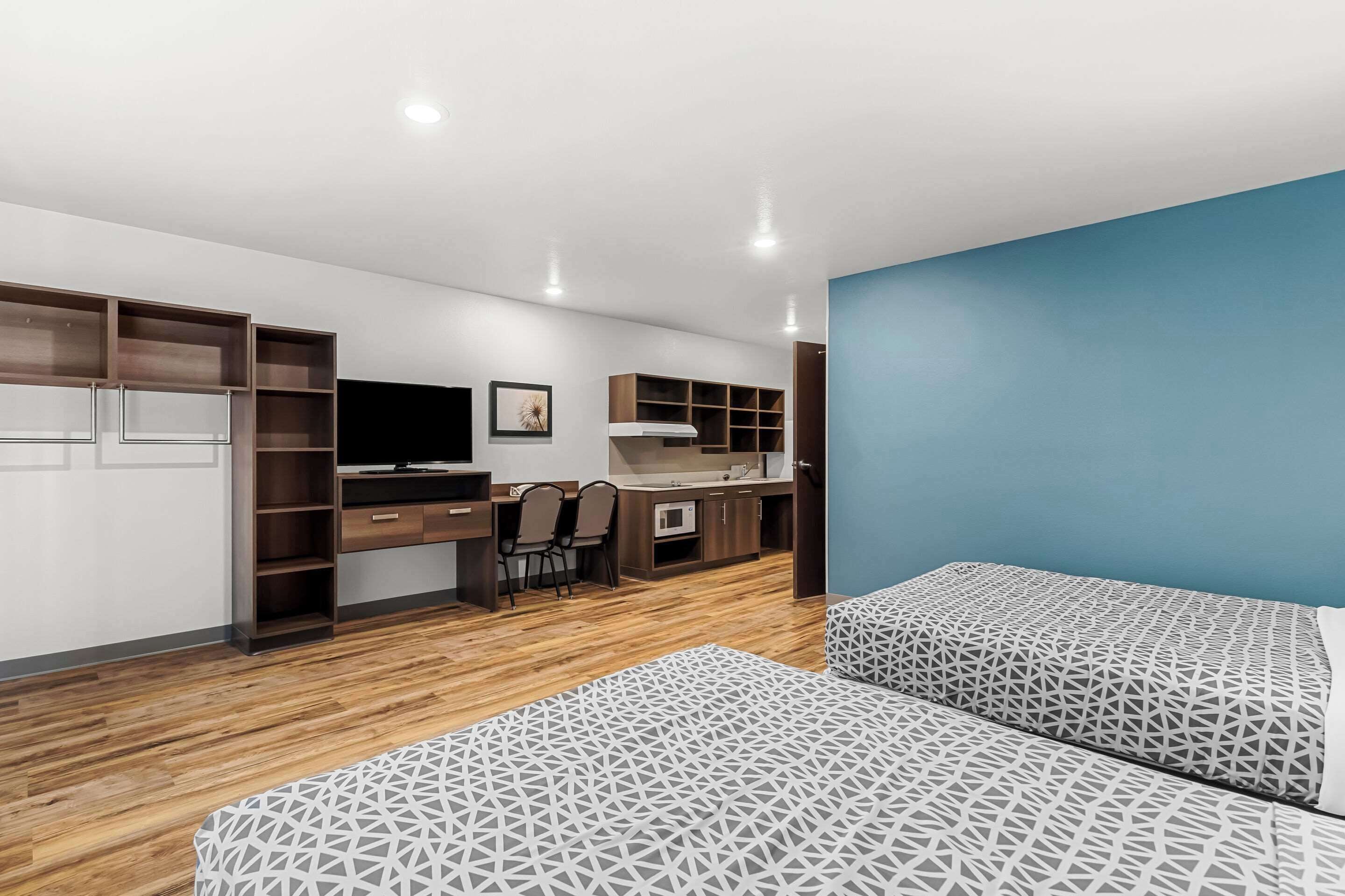 A modern room with a bed, a desk, and a kitchenette.