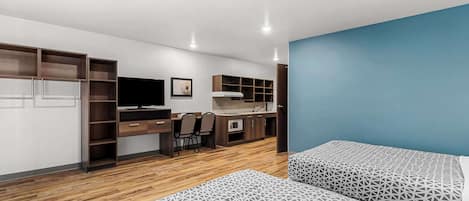 A modern room with a bed, a desk, and a kitchenette.