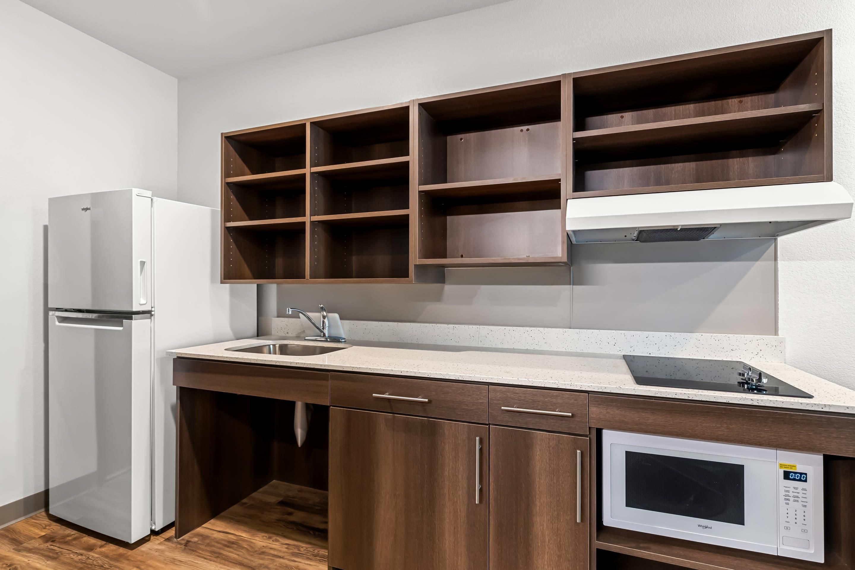A kitchen with a white refrigerator, a microwave, and wooden cabinets with open shelves.