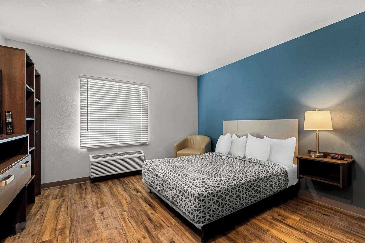 Un dormitorio con cama, una silla, mesita de noche, lámpara, calefactor y armario.