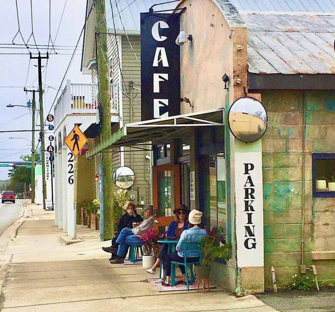 A cafe with outdoor seating, a pedestrian crossing sign, and a parking sign.