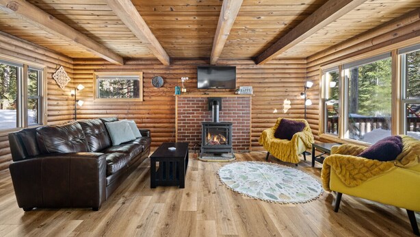 A cozy cabin interior with a fireplace, leather sofa, yellow armchair, and large windows. - Adorable Cabin 5-min walk to beach! Dog friendly! (Tahoe Vista)