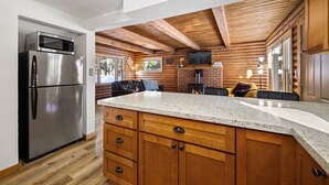 A kitchen with a stainless steel refrigerator, wooden cabinets, a granite countertop, and a fireplace. - Adorable Cabin 5-min walk to beach! Dog friendly! (Tahoe Vista)