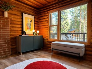 A cabin interior with a wooden interior, a bench, a cabinet, a framed picture, and a window with a view of trees and a deck.