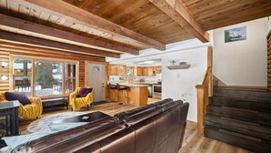 A cozy cabin interior with a wooden ceiling, a living area with a leather sofa and yellow armchair, a kitchen with wooden cabinets, and a staircase with a wooden railing. - Adorable Cabin 5-min walk to beach! Dog friendly! (Tahoe Vista)