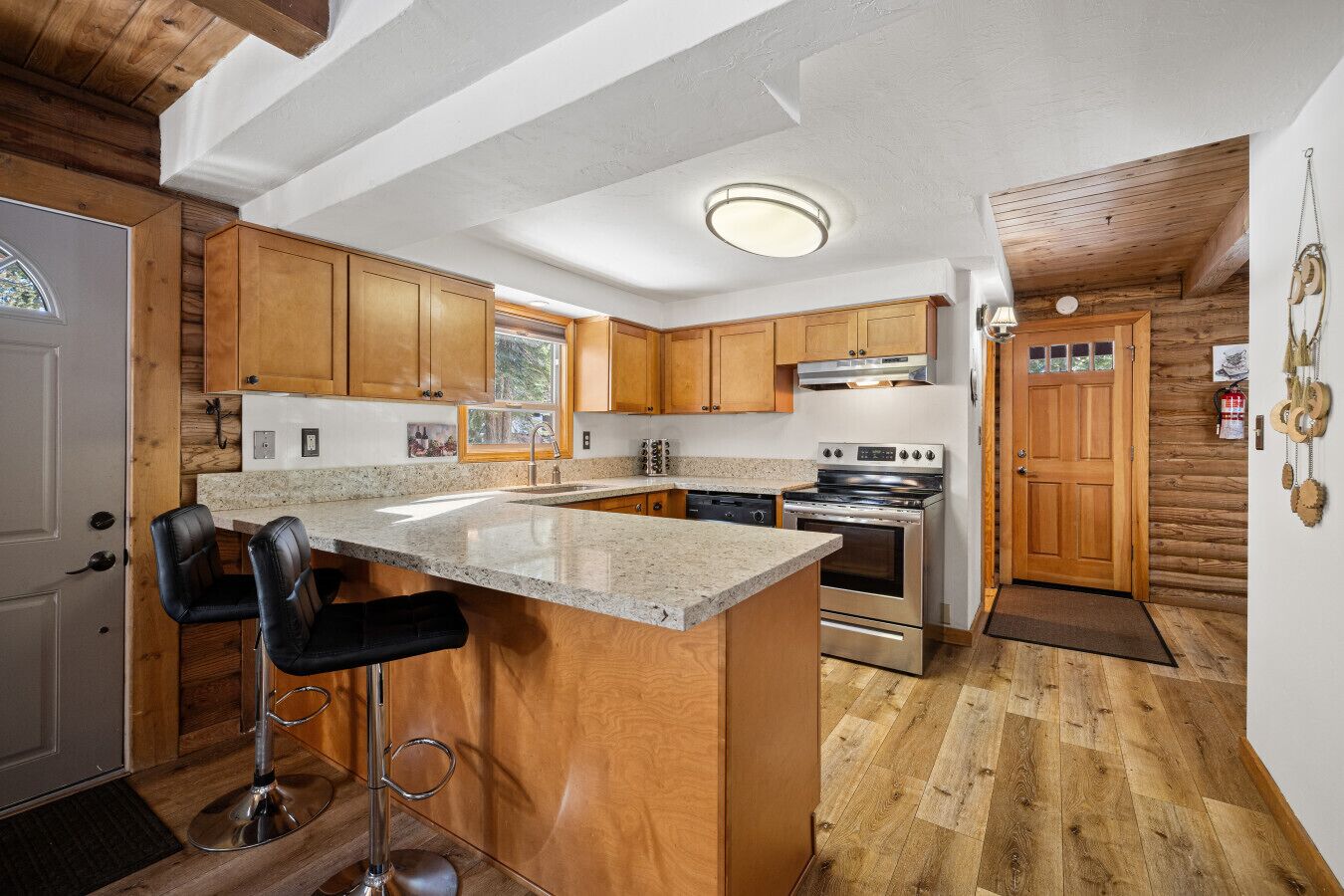 A kitchen with wooden cabinets, a granite countertop, stainless steel appliances, and a bar stool.