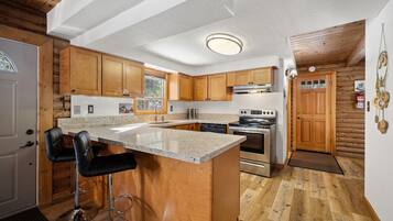 A kitchen with wooden cabinets, a granite countertop, stainless steel appliances, and a bar stool.