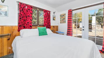 Un dormitorio con cama, ventana con cortinas rojas, cabecera de madera y puerta que da al exterior.