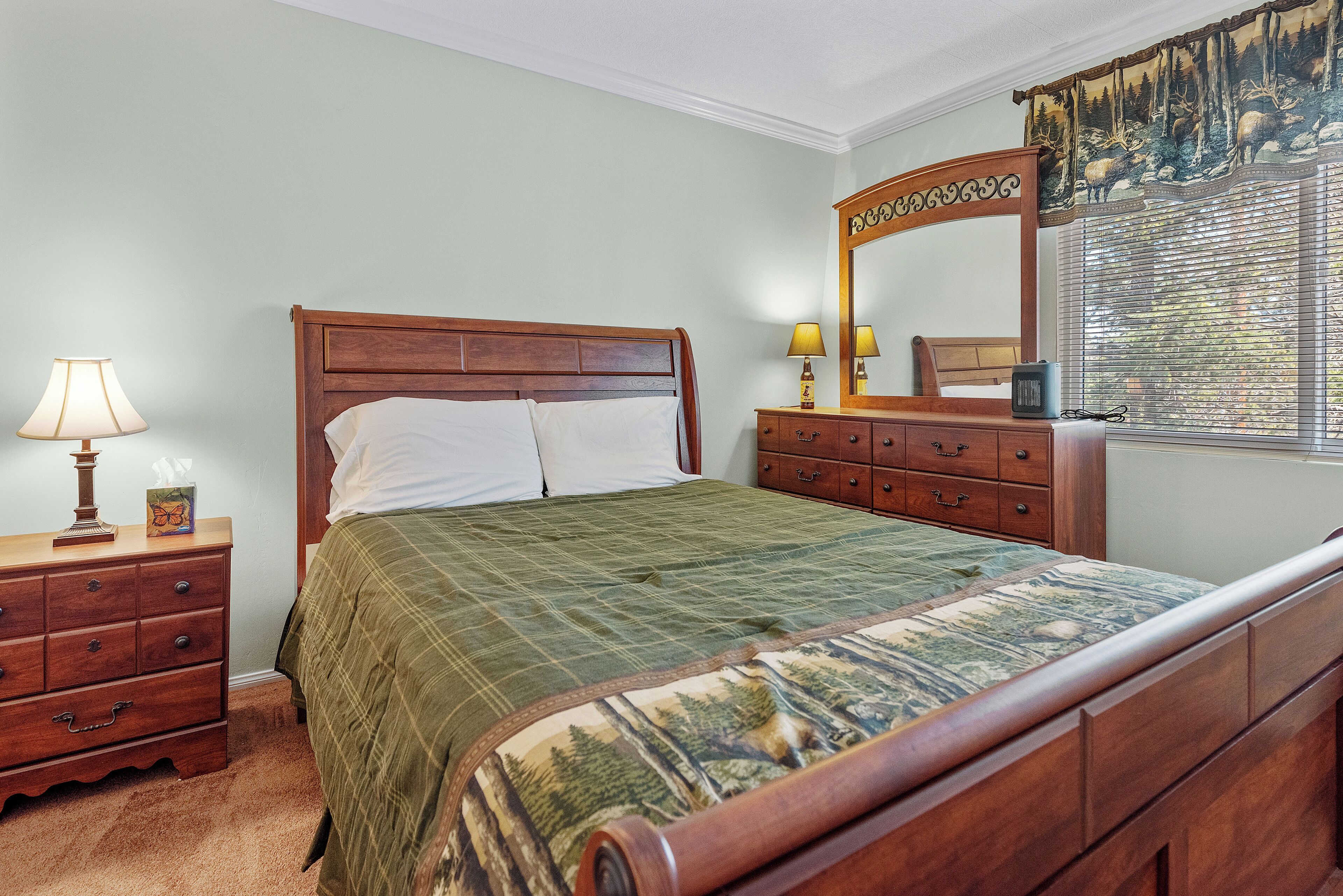 A bedroom with a wooden bed, a nightstand with a lamp, a dresser, and a mirror.