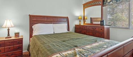 A bedroom with a wooden bed, a nightstand with a lamp, a dresser, and a mirror.