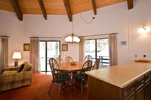A dining area with a wooden table and chairs, a chandelier, and a view through the glass doors. - Chamberlands Beach Home (Homewood)
