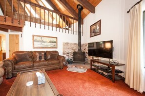 A cozy living room with a fireplace, leather sofa, television, and a wooden coffee table. - Chamberlands Beach Home (Homewood)