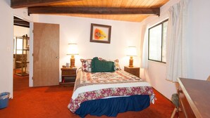 Una camera da letto con un letto, due comodini con lampade, una finestra con tende, una porta che dà su un'altra stanza e un quadro appeso al muro.