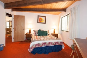 A bedroom with a bed, two bedside tables with lamps, a window with curtains, a door leading to another room, and a framed picture on the wall. - Chamberlands Beach Home (Homewood)