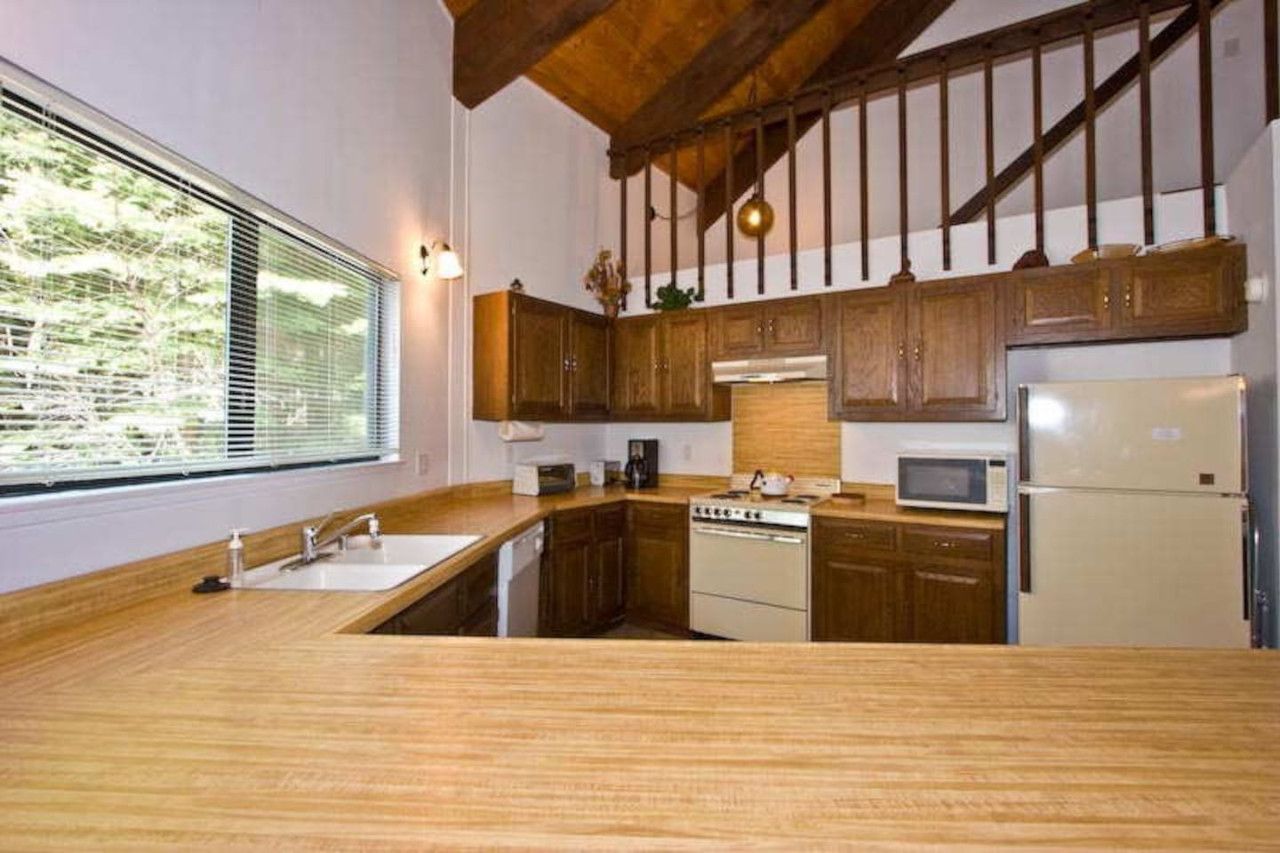 A kitchen with wooden cabinets, a sink, a stove, a microwave, and a refrigerator.