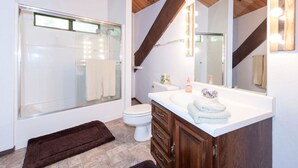 Un bagno moderno con cabina doccia in vetro, un water bianco, un lavabo con specchio e travi in legno al soffitto.