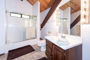A modern bathroom with a glass shower enclosure, a white toilet, a vanity with a mirror, and wooden beams on the ceiling. - Chamberlands Beach Home (Homewood)