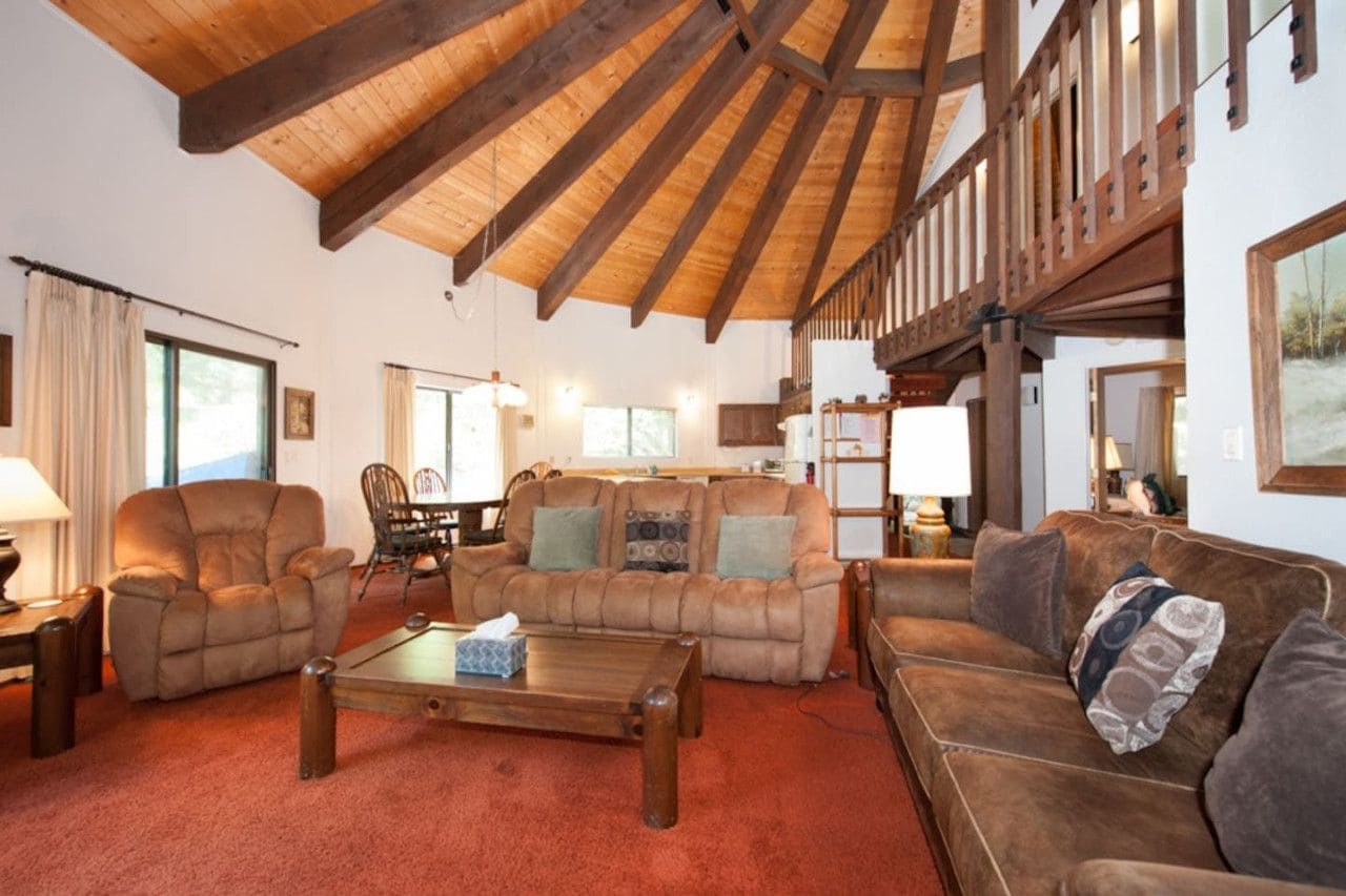 A spacious living room with a high wooden ceiling, leather sofas, a coffee table, and a dining area with chairs.