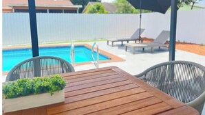 A wooden table with chairs and a black umbrella in a backyard with a swimming pool and lounge chairs. - Amazing bohemian house with a pool in a very nice neighborhood  (Sunrise)