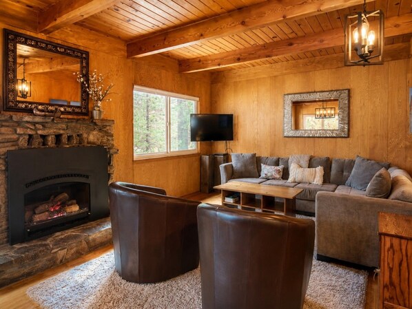 A cozy living room with a stone fireplace, leather seating, a flat-screen TV, and wooden walls.