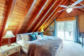 A bedroom with a sloped ceiling, a bed, a nightstand, a lamp, and a view of the outdoors.
