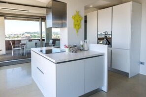Una cocina moderna con una isla central, muebles blancos y un amplio ventanal con vistas a un paisaje urbano.